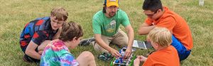 Michael Notaro sits in the grass working on a STEM project with student campers.