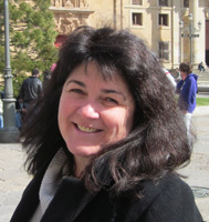 A portrait photo of Corinna Burger, who is smiling and has dark, shoulder-length hair and a black coat