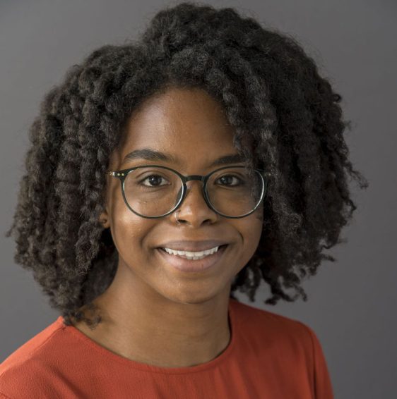 Morgan Jerald's profile picture. A Black woman with glasses and an orange shirt smiles at the camera against a grey background.