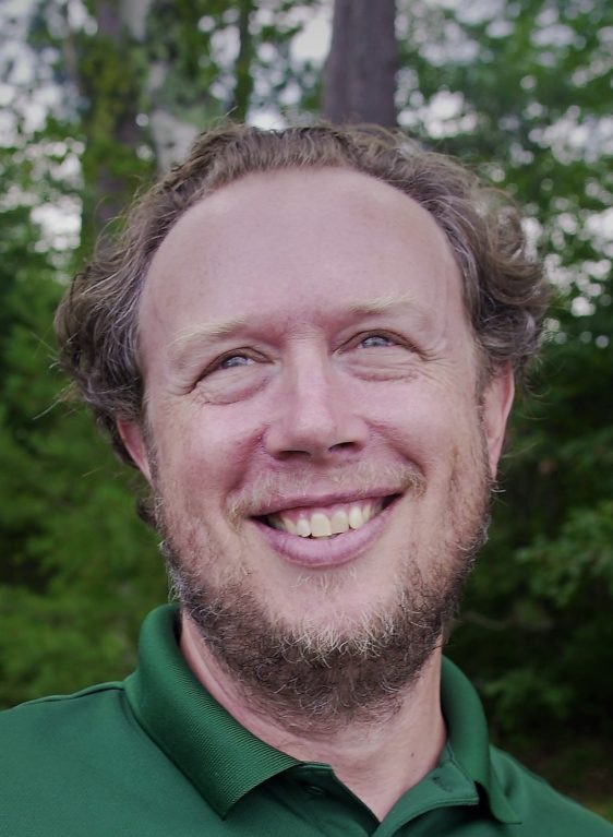 Olaf Jensen's profile picture. A smiling white man in a green shirt against a background of green leaves.